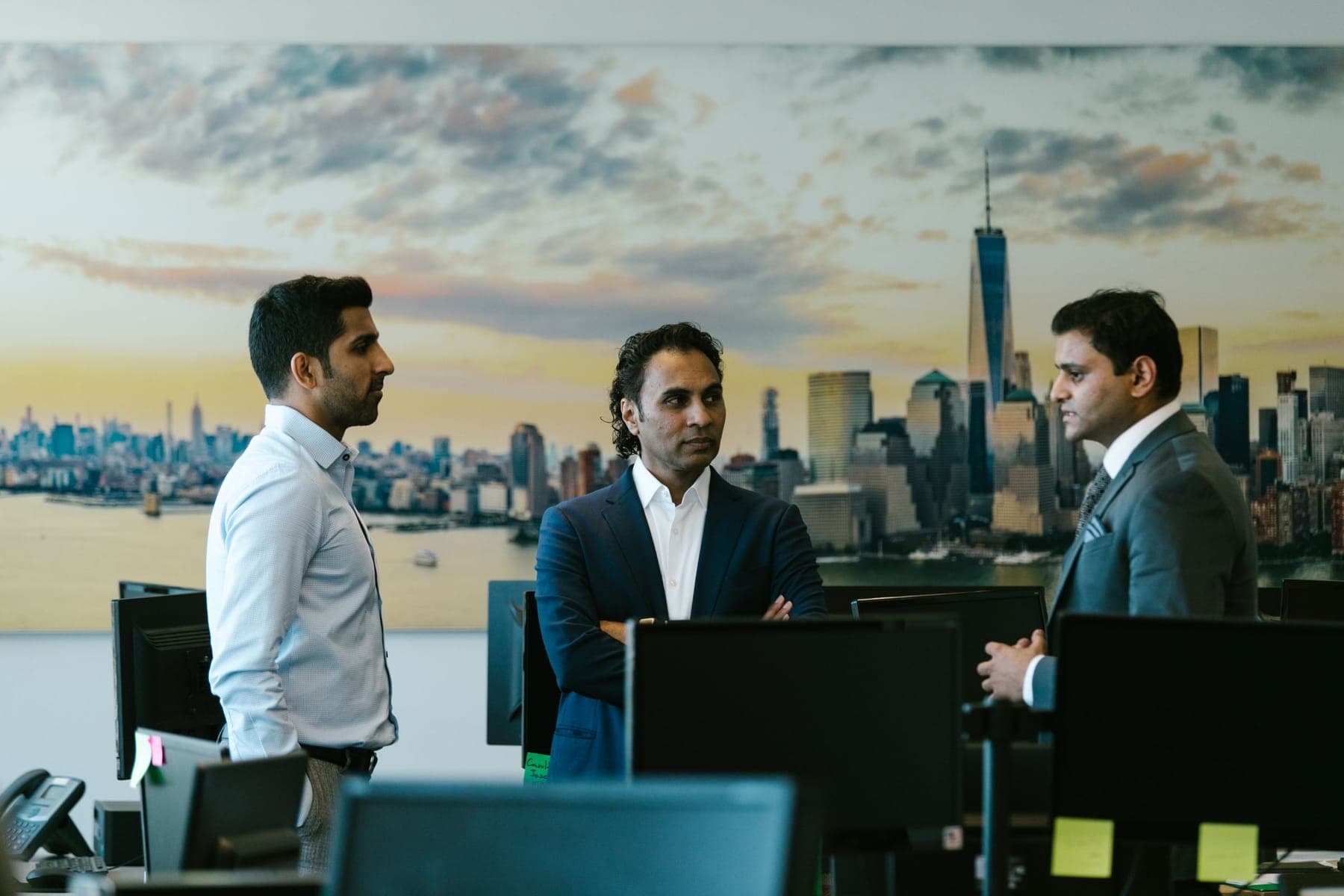 Three colleagues talking in an office, a city skyline behind them