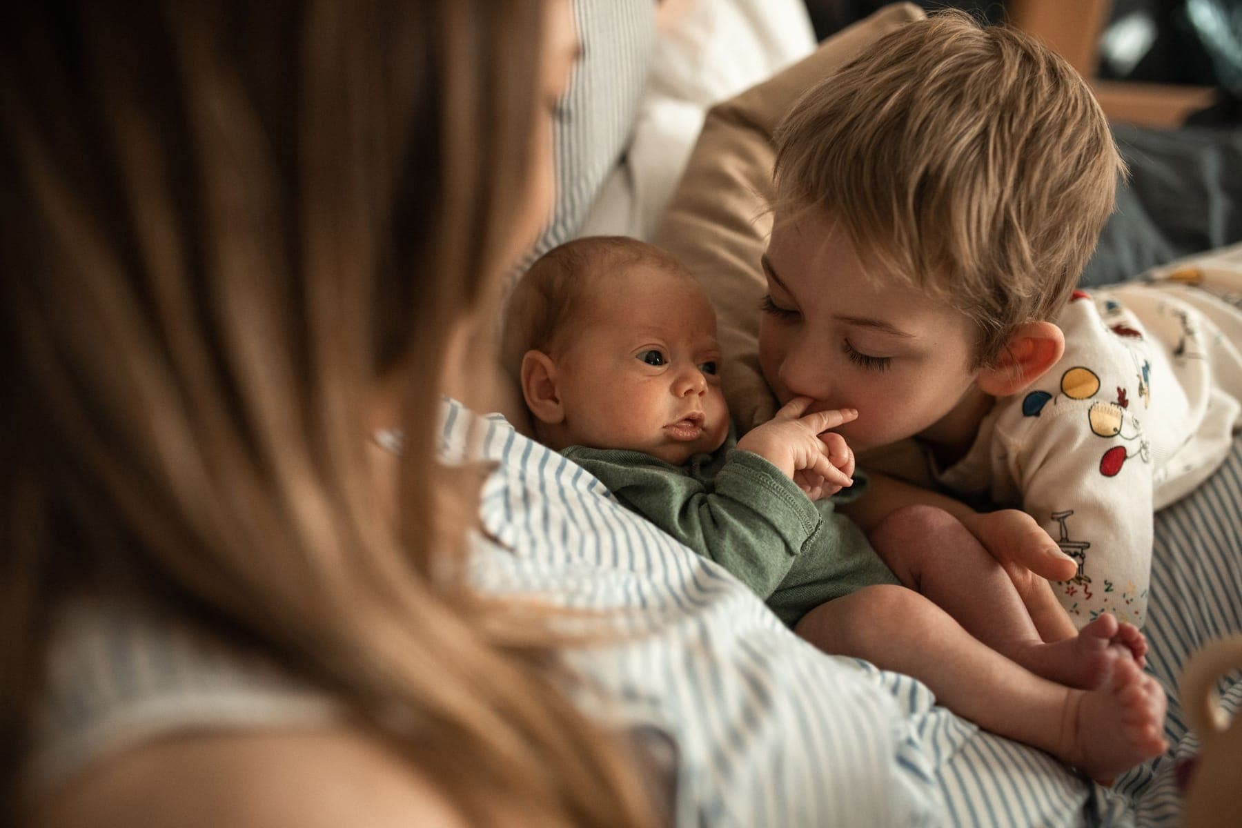 A mother holding a baby while a toddler leans in close