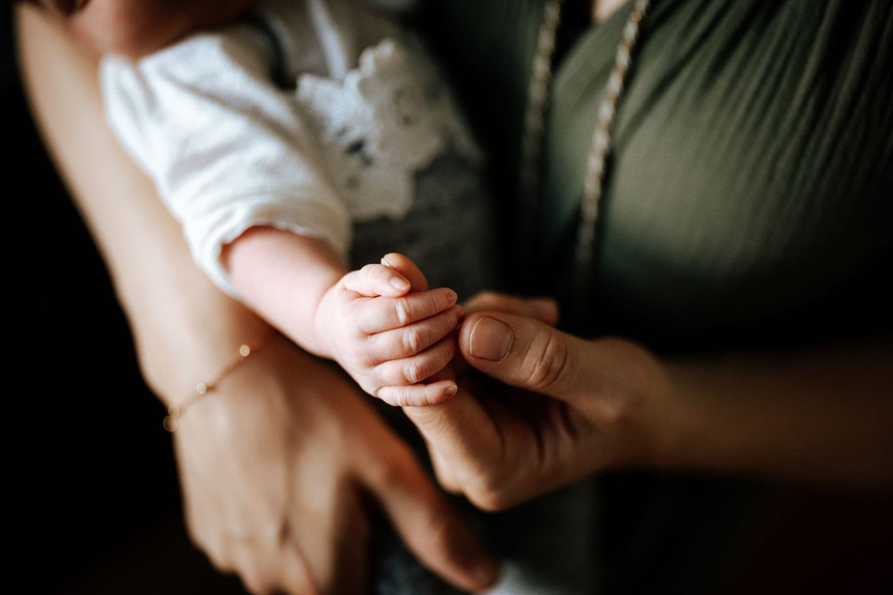 A newborn’s hand held between two adult hands