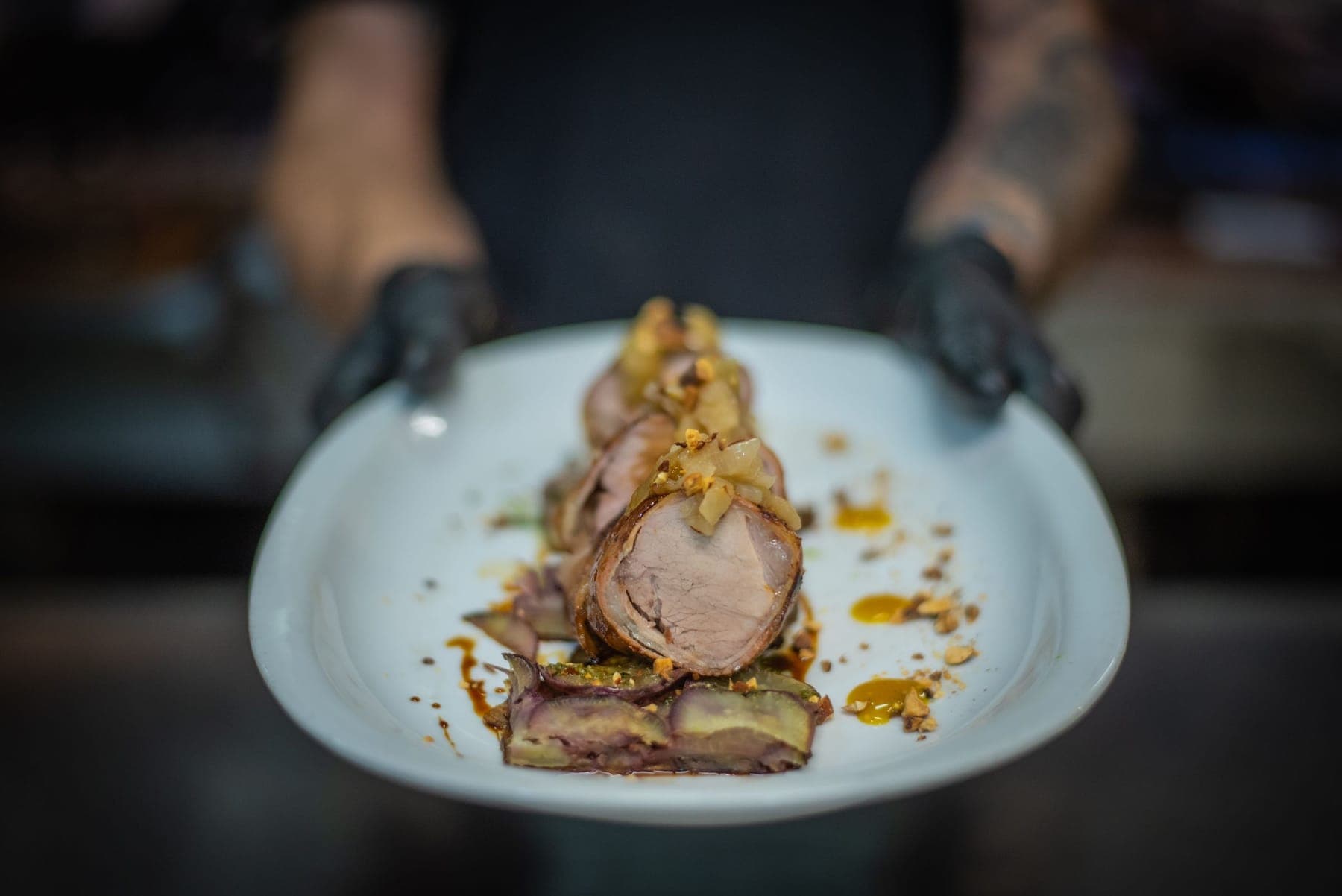 A chef presenting a plate, hands in black gloves