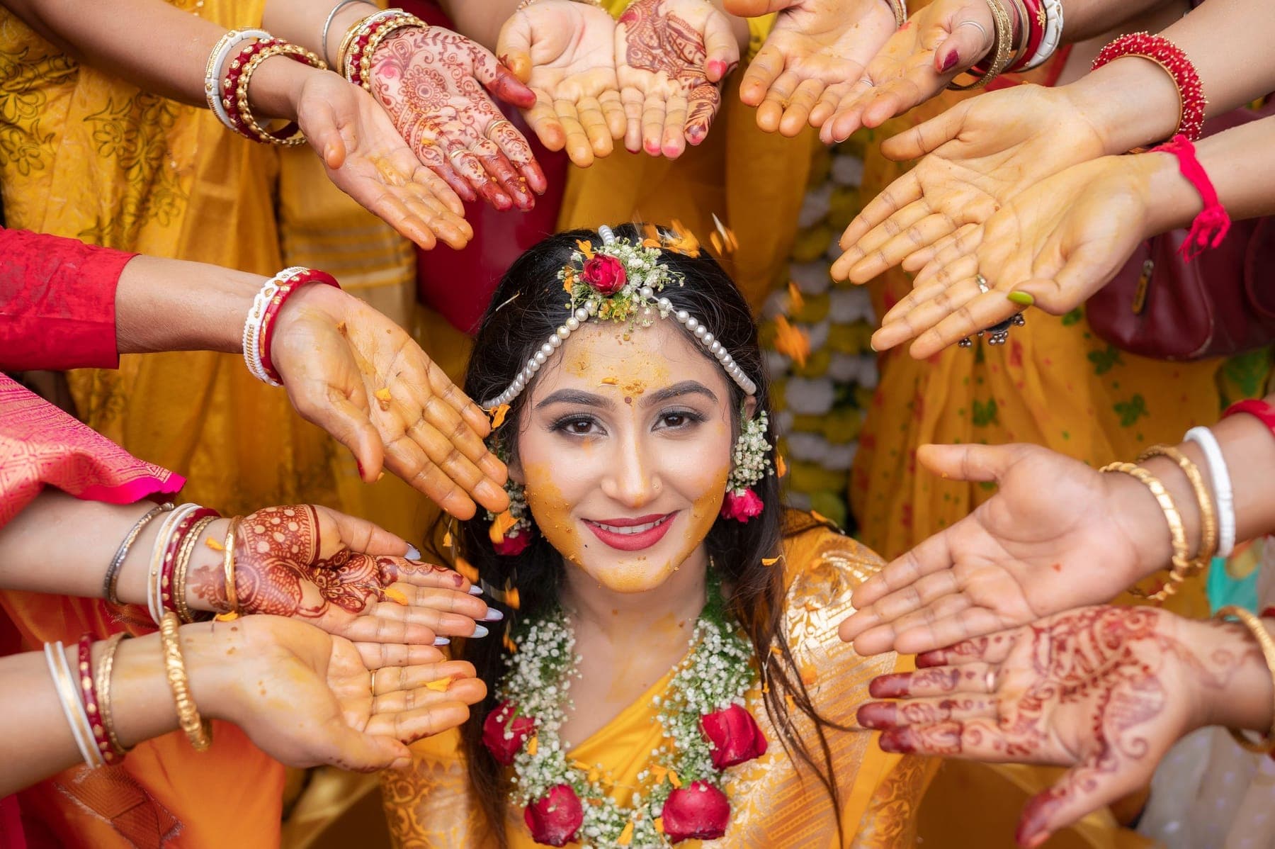 A bride at her mehndi, ringed by the hennaed hands of her friends
